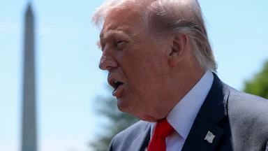 Donald Trump, seen in profile, speaks to reporters outside the White House. The Washington Monument is in the background.