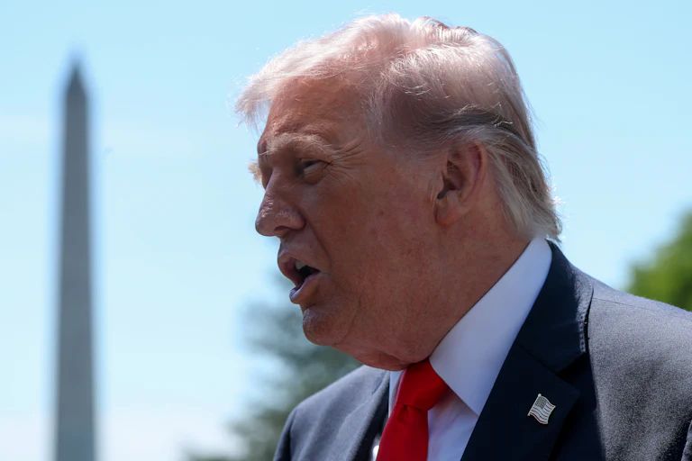 Donald Trump, seen in profile, speaks to reporters outside the White House. The Washington Monument is in the background.