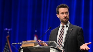 Charles Allen gesticulates while speaking at a podium.