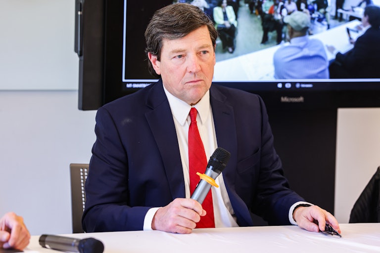 Ed Martin holds a mic and sits at a table.