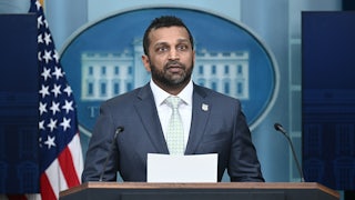FBI Director Kash Patel speaks at the podium in the White House press briefing room, holding papers in hand.