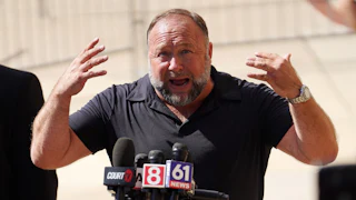Alex Jones gestures and speaks into reporters' microphones