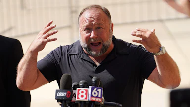 Alex Jones gestures and speaks into reporters' microphones