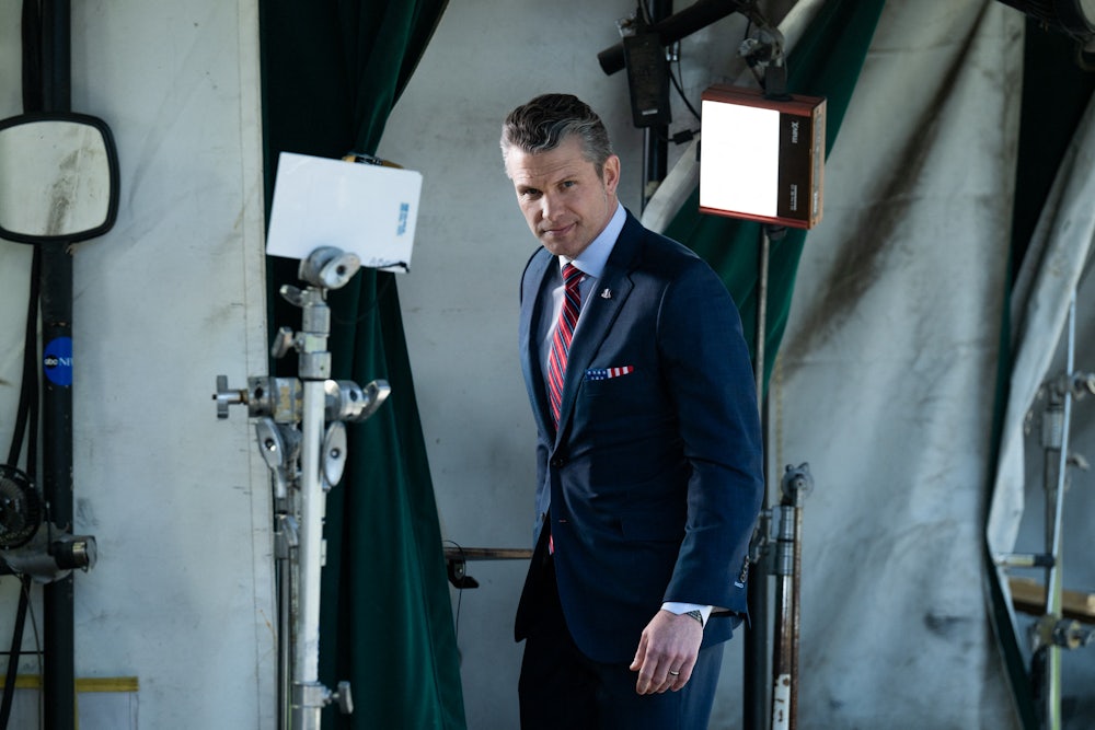 Defense Secretary Pete Hegseth stands in front of some teleprompters