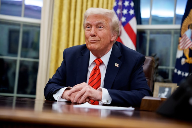Donald Trump smiles while sitting at his desk in the Oval Office