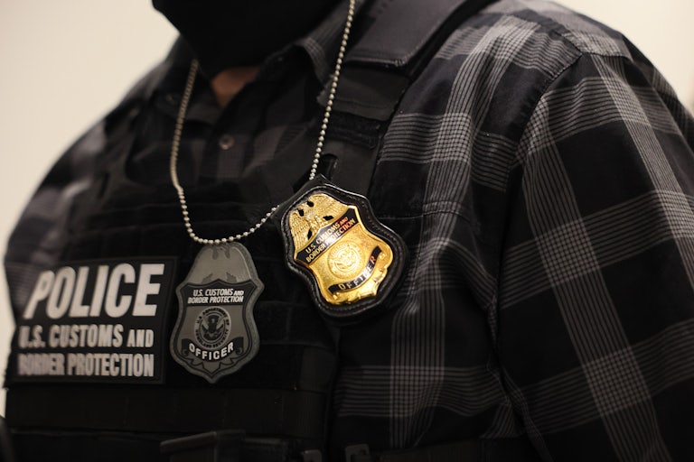 An immigration enforcement officer wears a tactical vest and badges