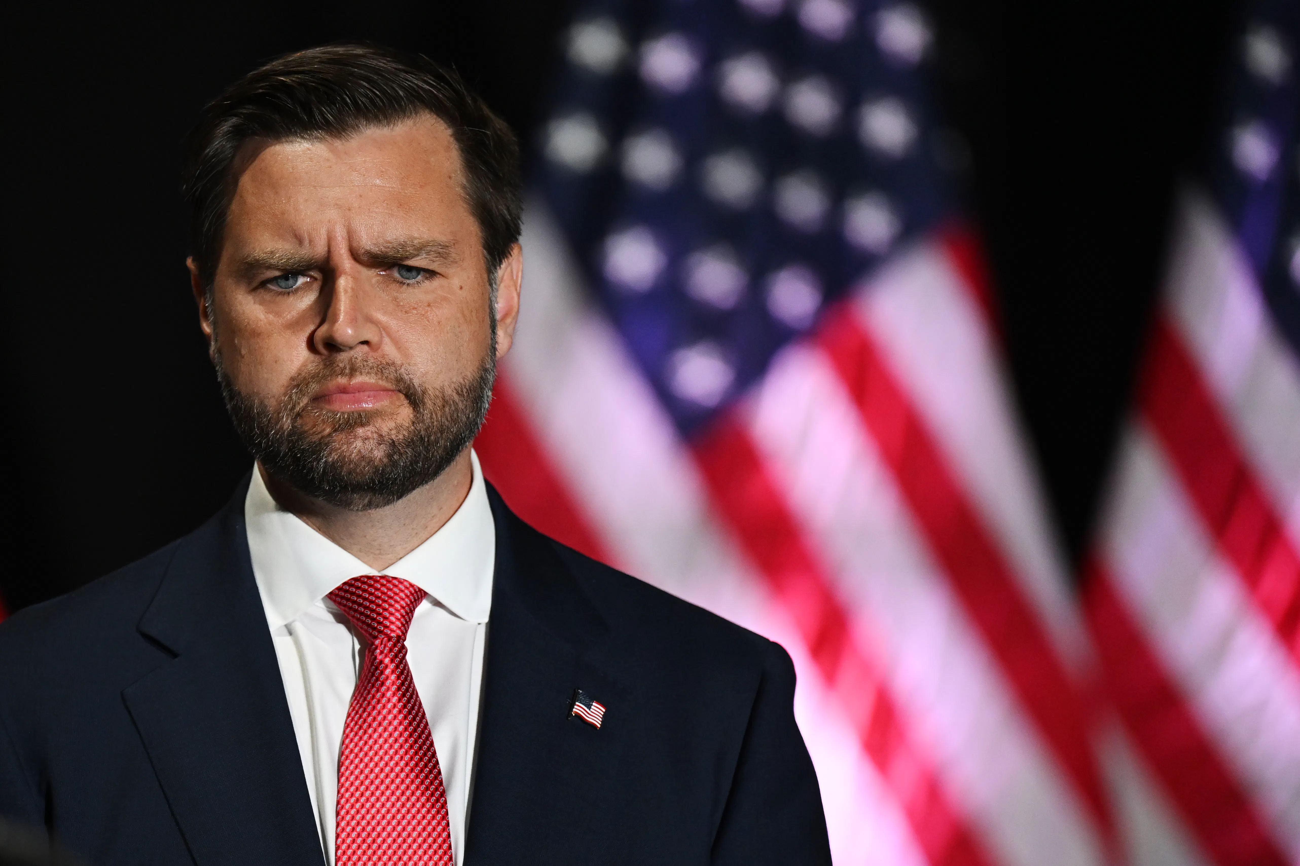 JD vance looks confused while standing in front of a US flag