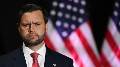 JD vance looks confused while standing in front of a US flag