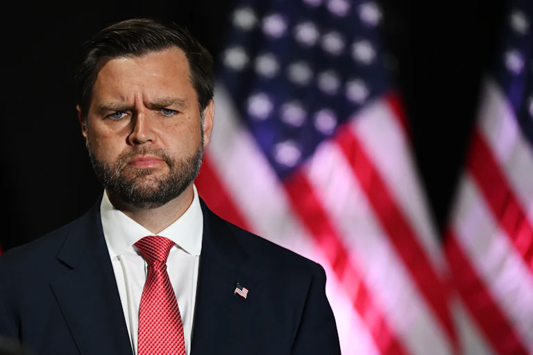JD vance looks confused while standing in front of a US flag