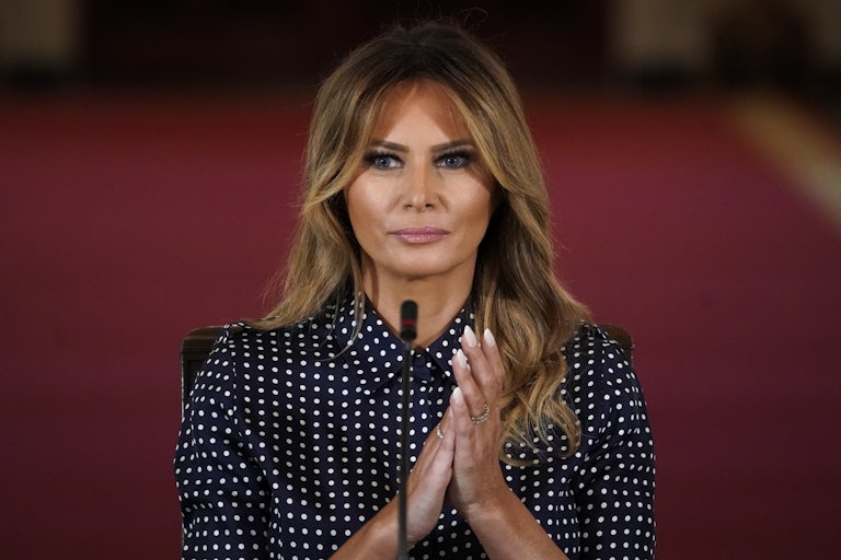 Melania Trump clasps her hands while wearing a polka dot blouse