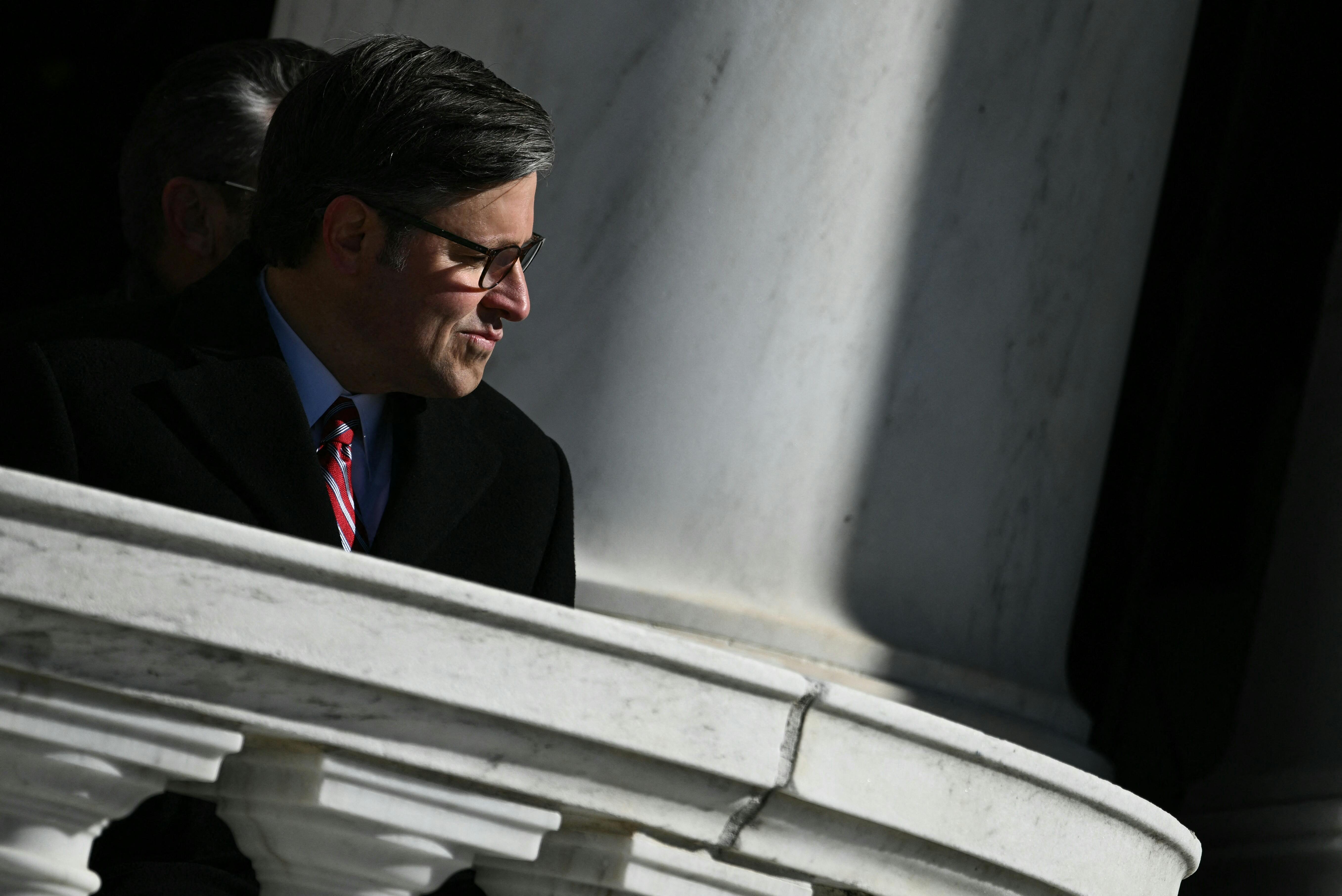 House Speaker Mike Johnson pushes his mouth the side while sitting during a ceremony at Arlington National Cemetery