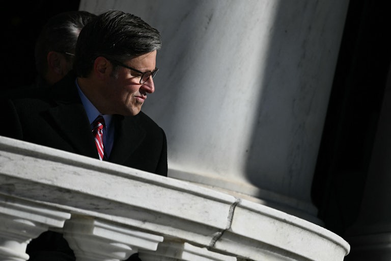 House Speaker Mike Johnson pushes his mouth the side while sitting during a ceremony at Arlington National Cemetery