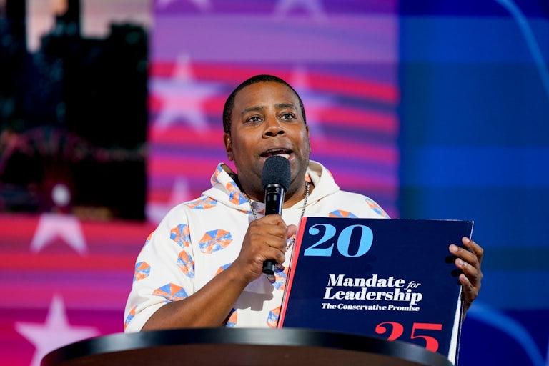 Kenan Thompson speaks into a microphone while holding a copy of Project 2025 at the Democratic National Convention