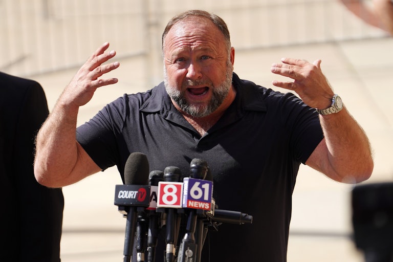 Alex Jones gestures as he speaks into microphones