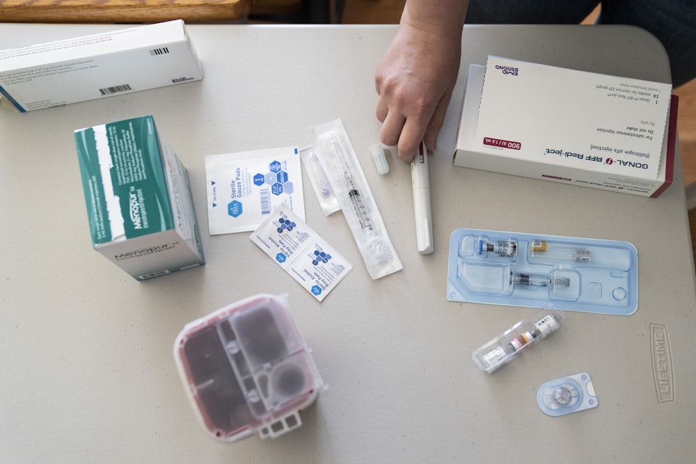 A hand hovers over an assortment of syringes, vials of fertility drugs, and alcohol wipes.