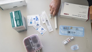 A hand hovers over an assortment of syringes, vials of fertility drugs, and alcohol wipes.