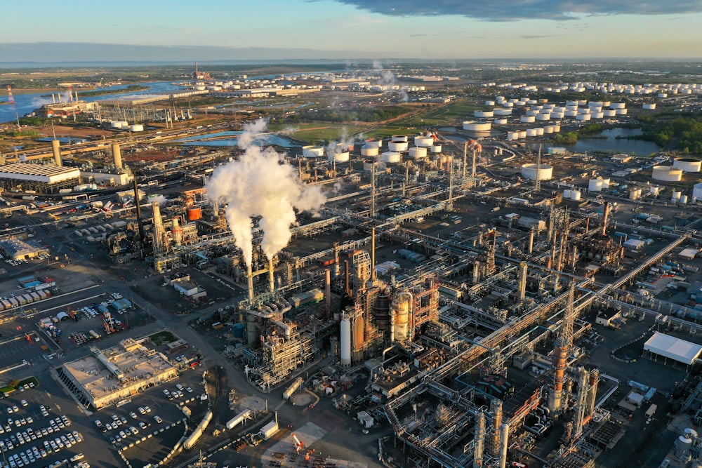 A refinery with smokestacks sits near a river.