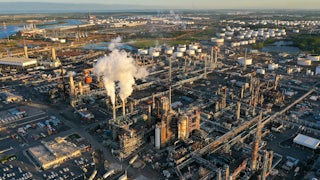 A refinery with smokestacks sits near a river.