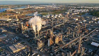 A refinery with smokestacks sits near a river.