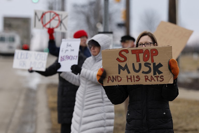 A protester holds up a sign that says, "Stop Musk and his rats"