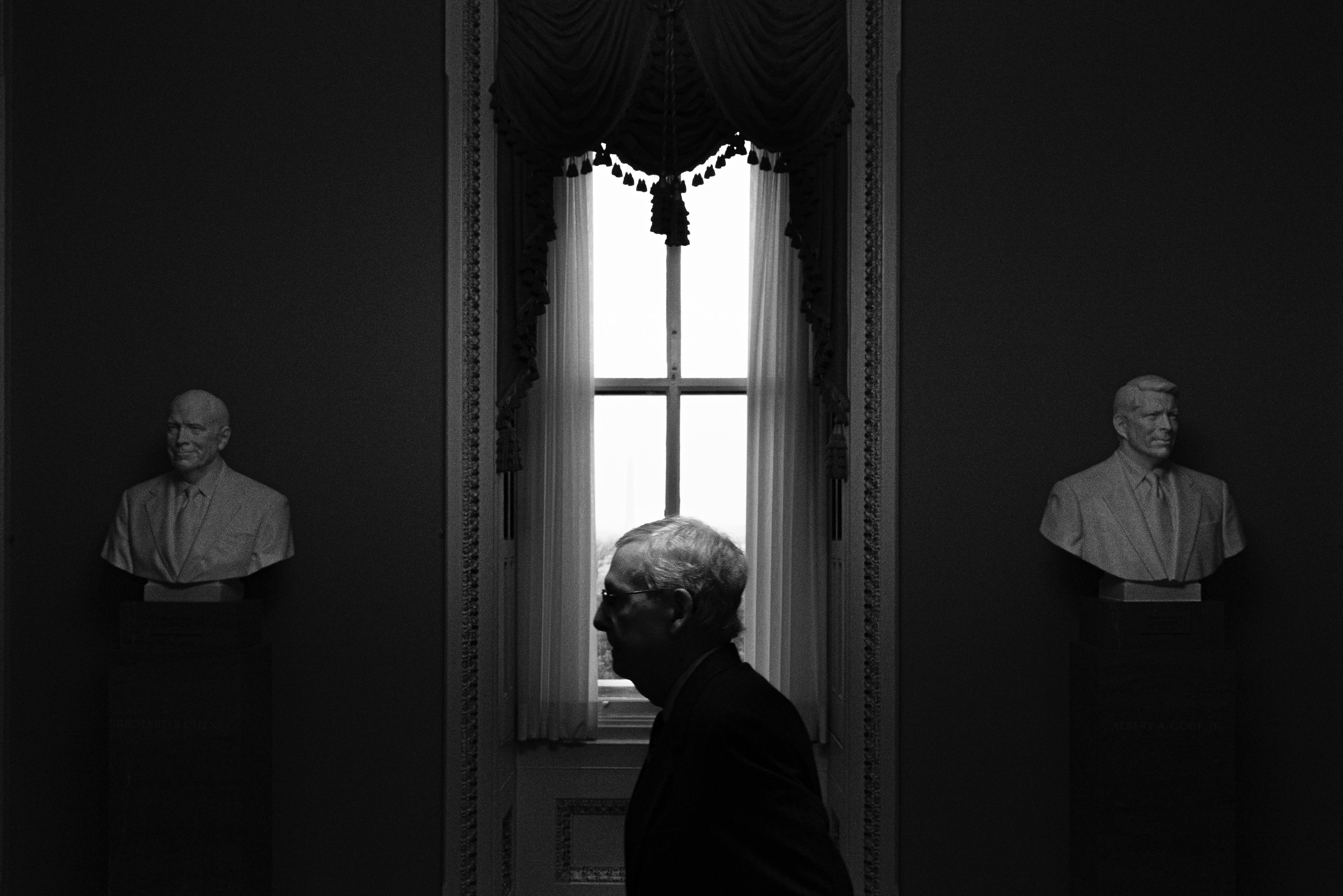 The black and white image Senate Minority Leader Mitch McConnell's profile is seen framed by a window, between two pieces of statuary.