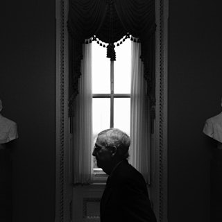 The black and white image Senate Minority Leader Mitch McConnell's profile is seen framed by a window, between two pieces of statuary.