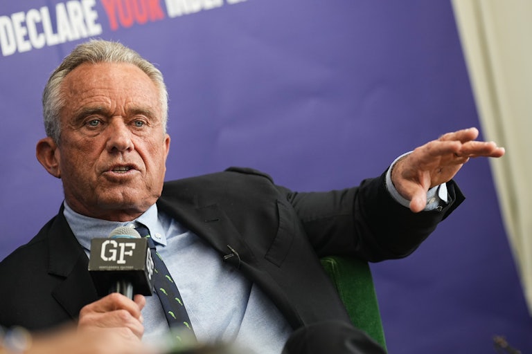 Robert F. Kennedy Jr. speaks, holding a mic with one hand and making a hand gesture with the other