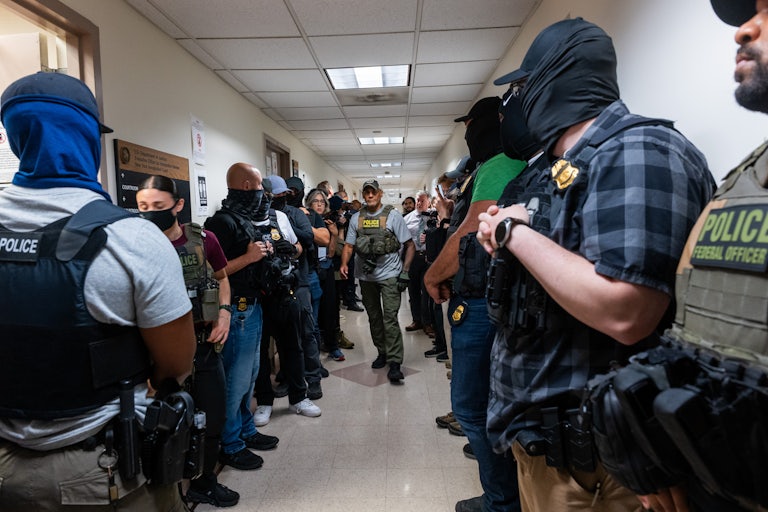 Nearly 20 immigration agents crowd the hallway in immigration court. Most are wearing masks.