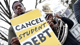 a man holds a sign reading "cancel student debt" while another man plays the tuba