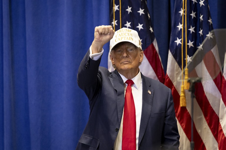 Donald Trump raises his first while wearing a baseball cap.