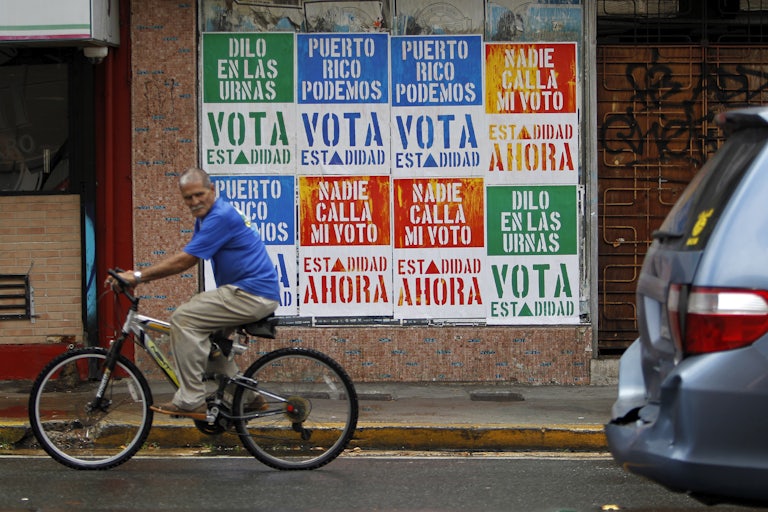 A man rides his bicycle in front of a wall covered with campaign posters promoting Puerto Rico’s statehood