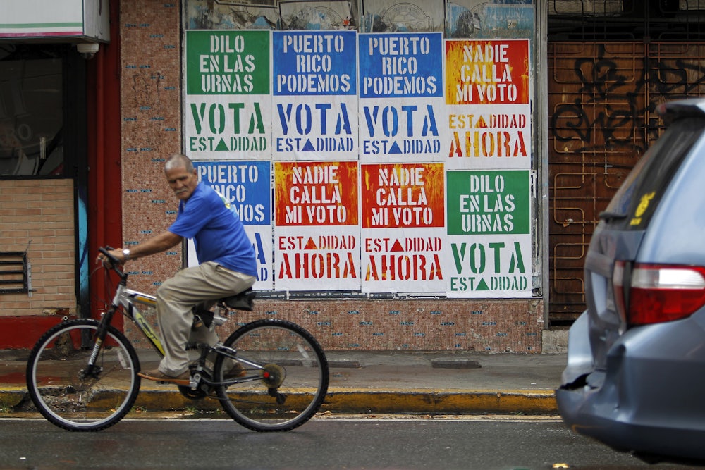 A man rides his bicycle in front of a wall covered with campaign posters promoting Puerto Rico’s statehood