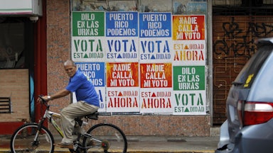 A man rides his bicycle in front of a wall covered with campaign posters promoting Puerto Rico’s statehood