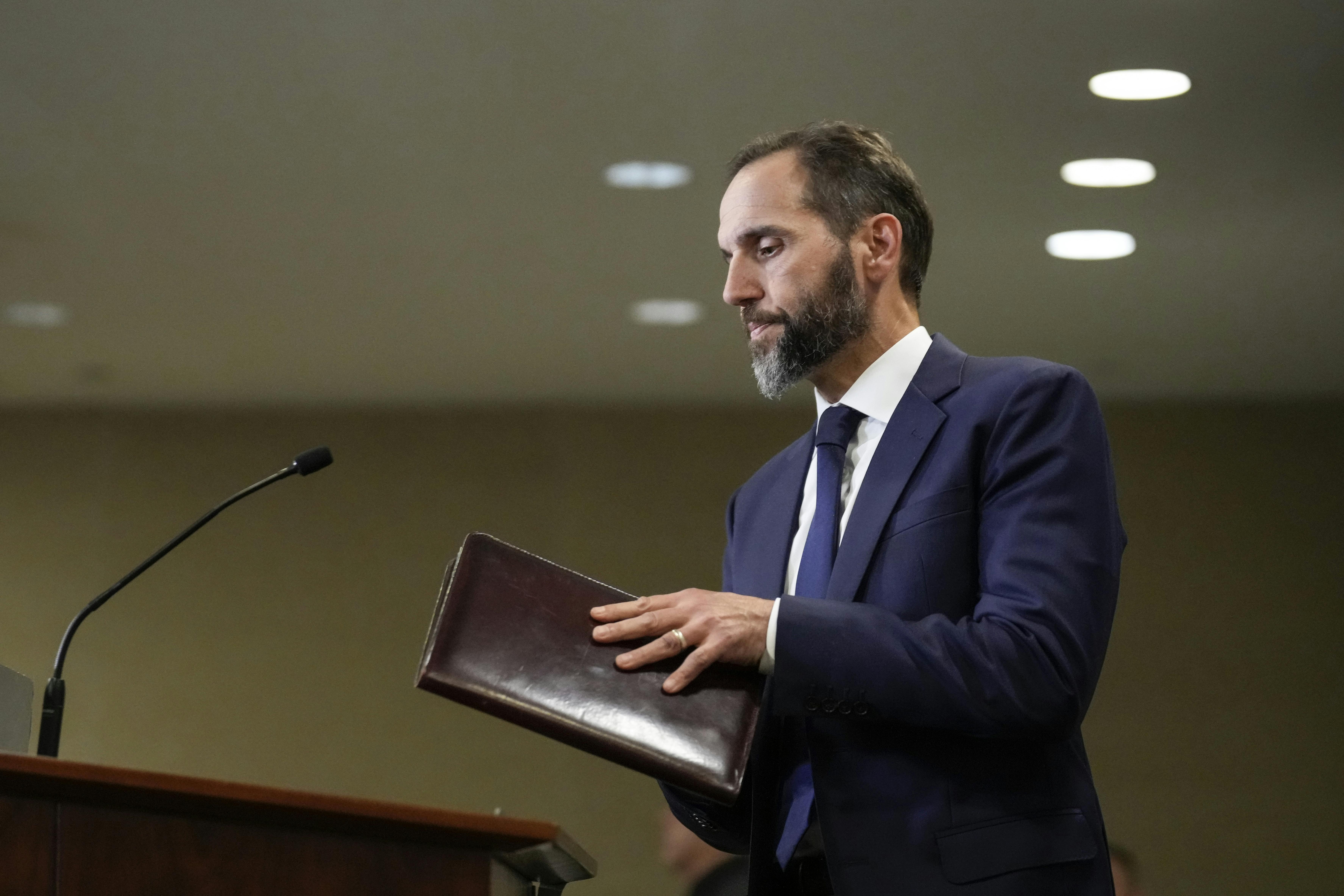 Special counsel Jack Smith holds a folder and walks toward a podium.