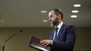 Special counsel Jack Smith holds a folder and walks toward a podium.