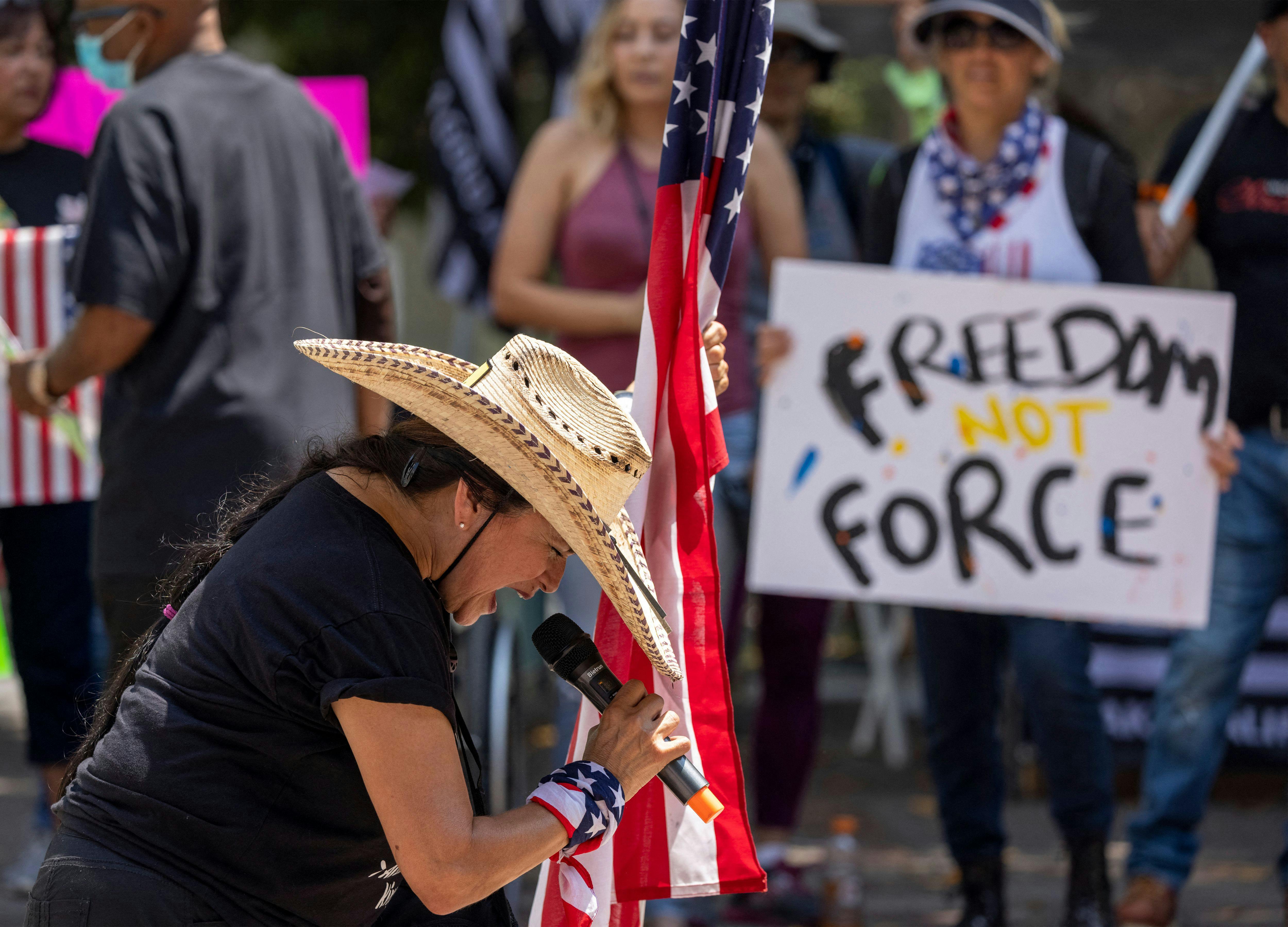 A woman holds an American flag and prays at an anti-vaccine rally in Los Angeles.