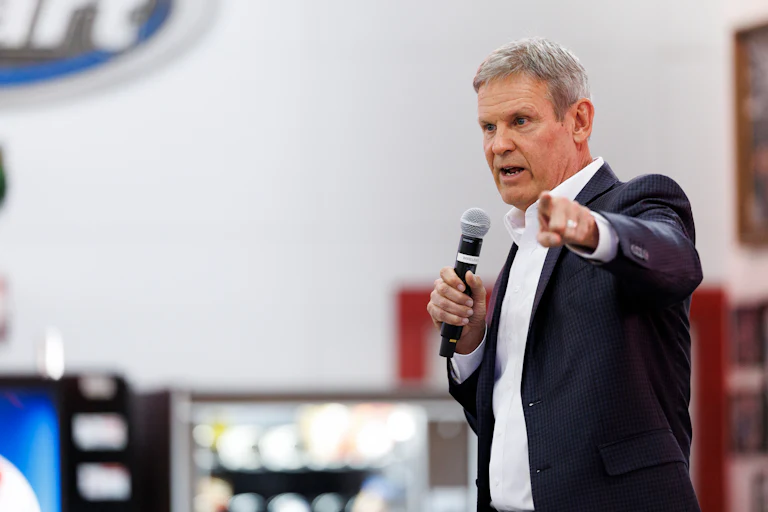 Tennessee Governor Bill Lee talks into a handheld microphone while standing and gesticulating.