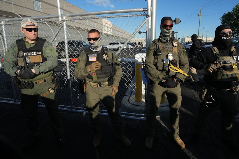 Four ICE agents (three white men, one Black man) all wear full protective gear and face masks.