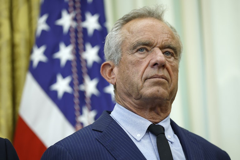 Robert F. Kennedy Jr., wearing a suit and tie, stands in front of American flags at the White House.