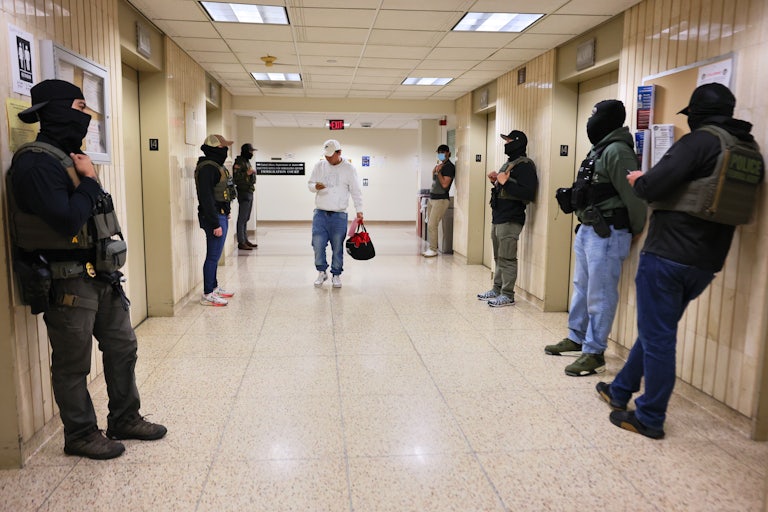 Seven masked federal agents line up against the walls at a courthouse in New York City, prepared to detain immigrants.