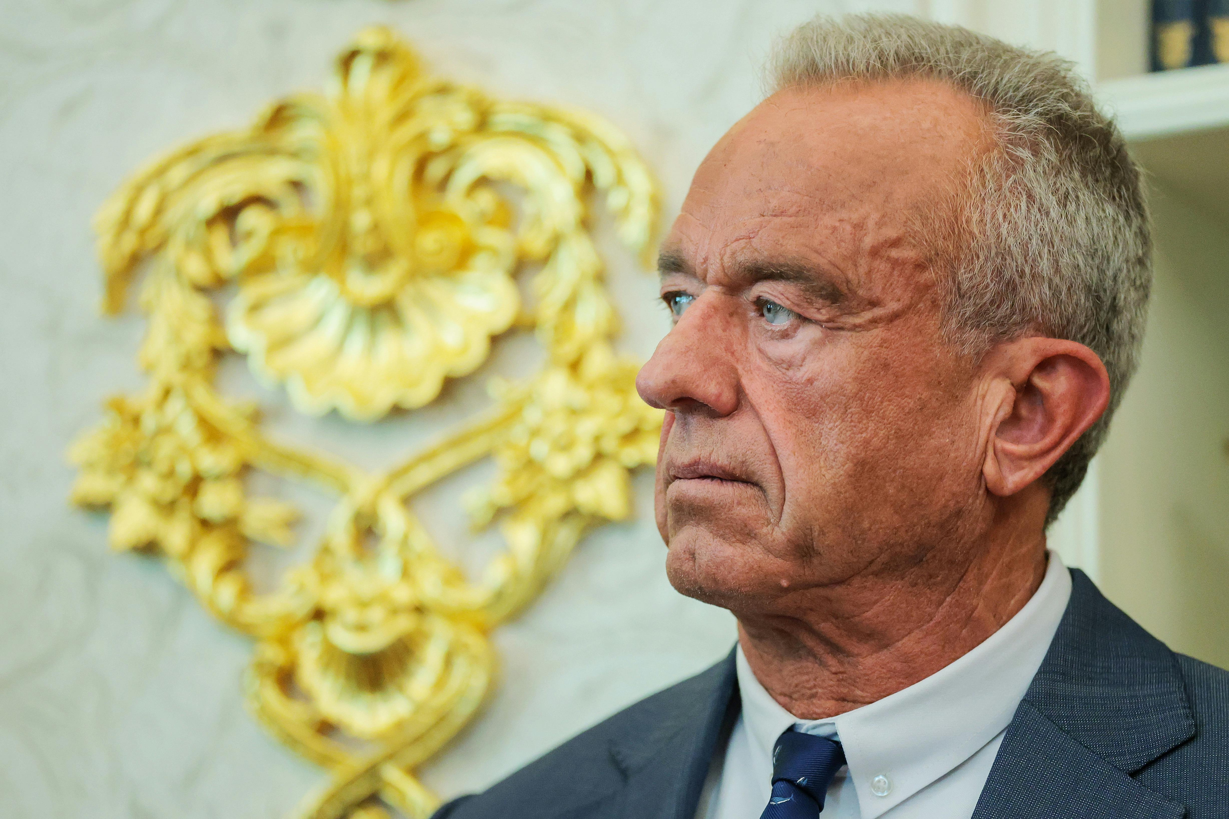 Robert F. Kennedy Jr. stands in front of a gold embellishment on the wall of the White House Oval Office.