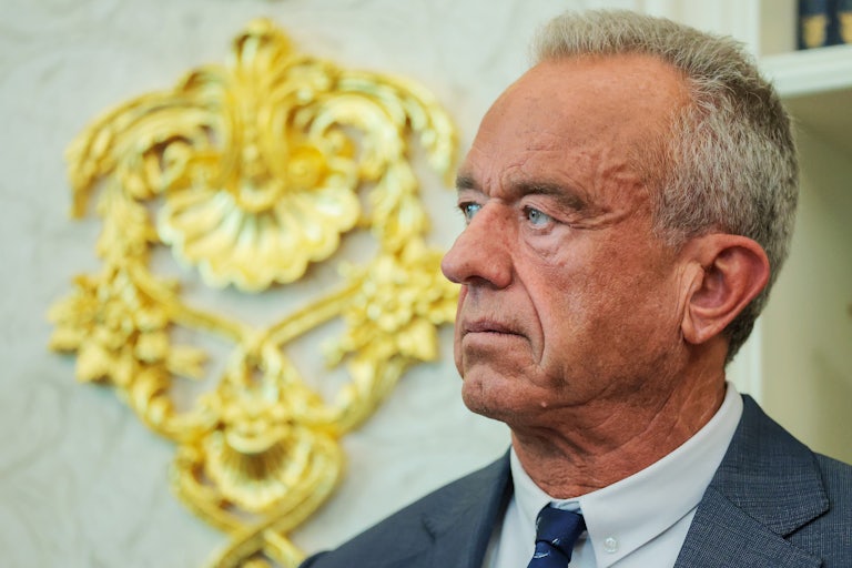 Robert F. Kennedy Jr. stands in front of a gold embellishment on the wall of the White House Oval Office.