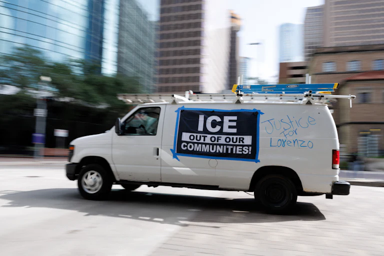 A van with a banner on the side that says "ICE out of our communities!" and writing on the side that says "Justice for Lorenzo"