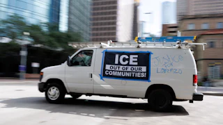 A van with a banner on the side that says "ICE out of our communities!" and writing on the side that says "Justice for Lorenzo"
