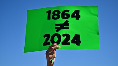 A protestor holds a sign reading 1864 does not equal 2024