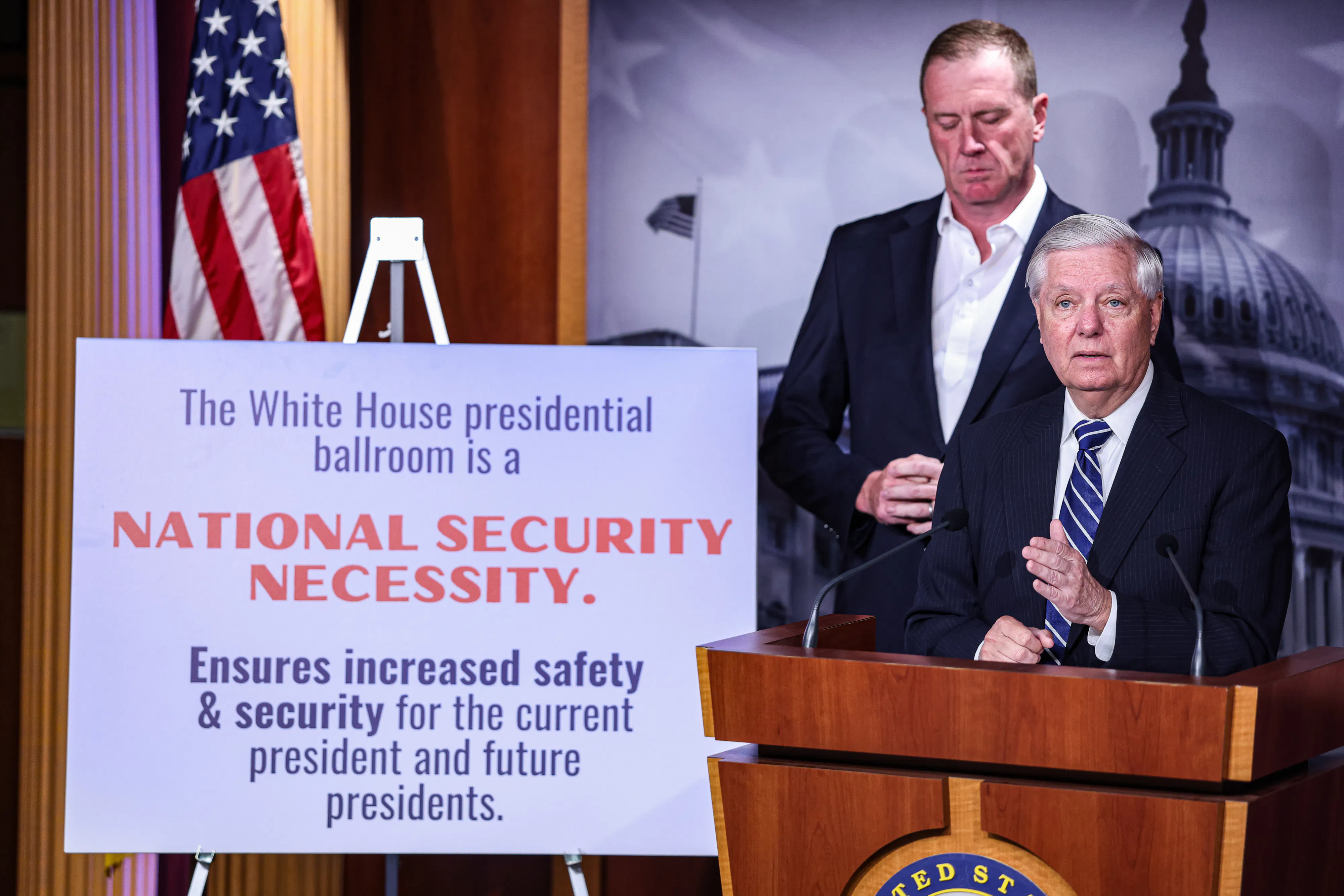 Senator Lindsey Graham speaks at a podium next to a sign describing why Donald Trump's ballroom is needed for national security