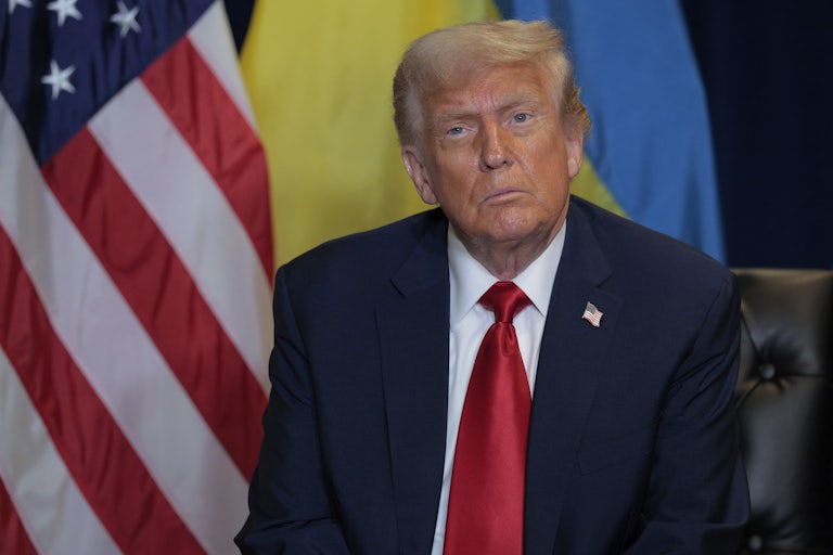 Donald Trump sits in front of an American and a Ukrainian flag