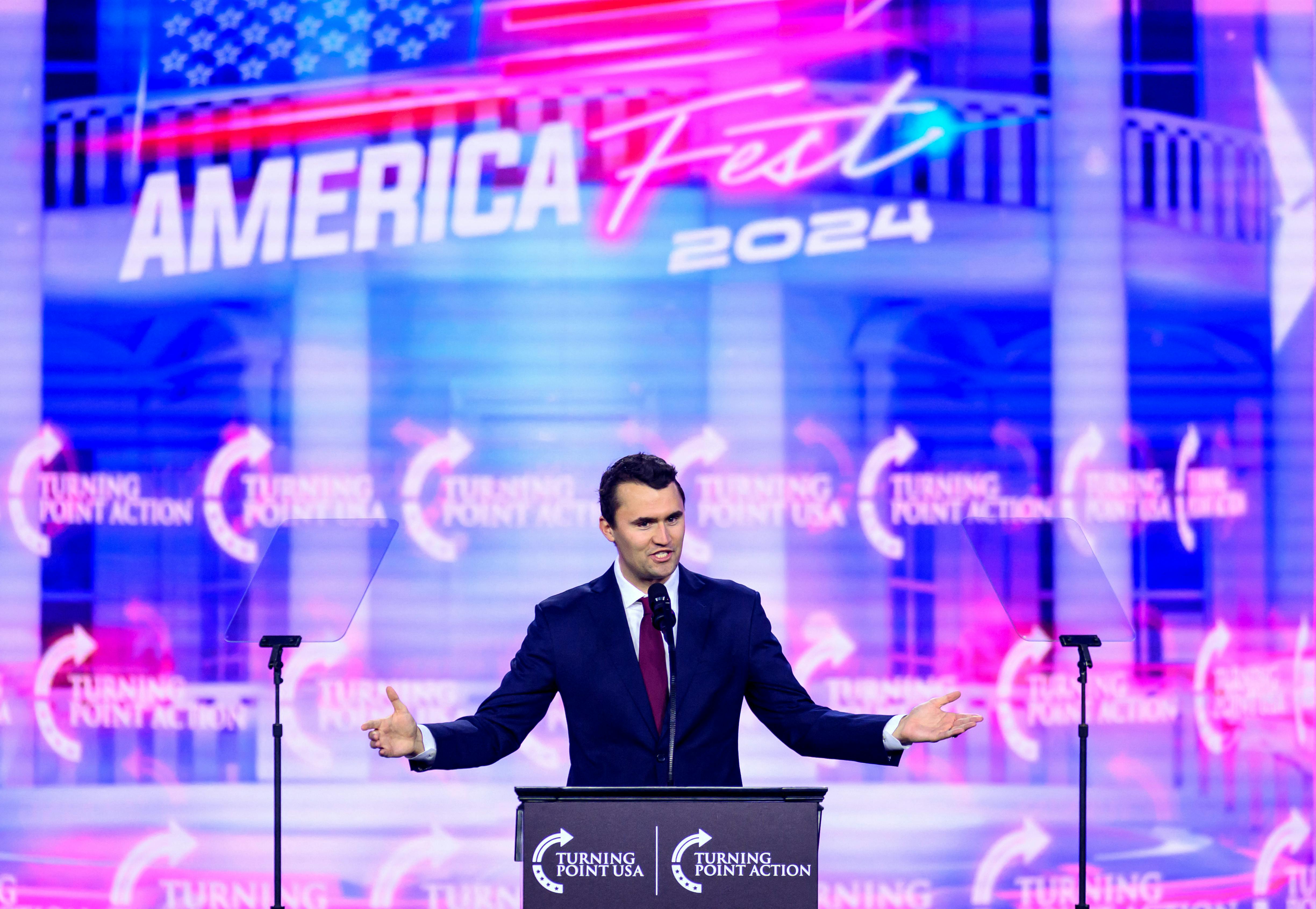 Charlie Kirk holds his arms out to the side while speaking onstage at AmericaFest 2024