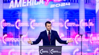 Charlie Kirk holds his arms out to the side while speaking onstage at AmericaFest 2024