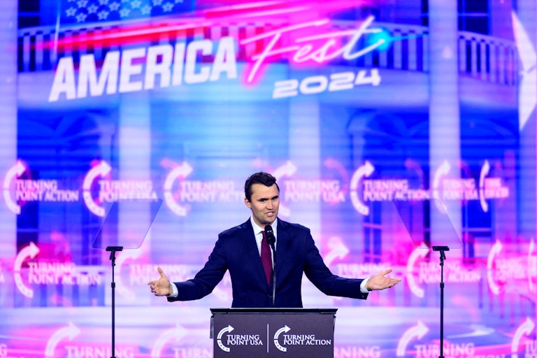 Charlie Kirk holds his arms out to the side while speaking onstage at AmericaFest 2024